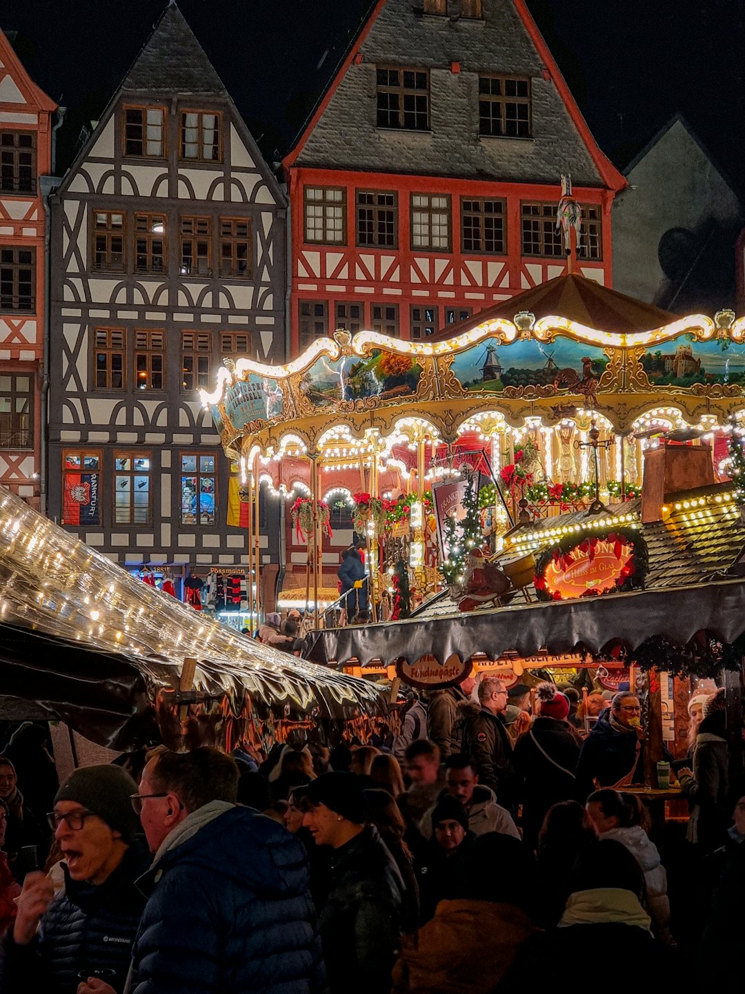 Menschen versammeln sich um ein hell erleuchtetes Karussell auf einem Weihnachtsmarkt.