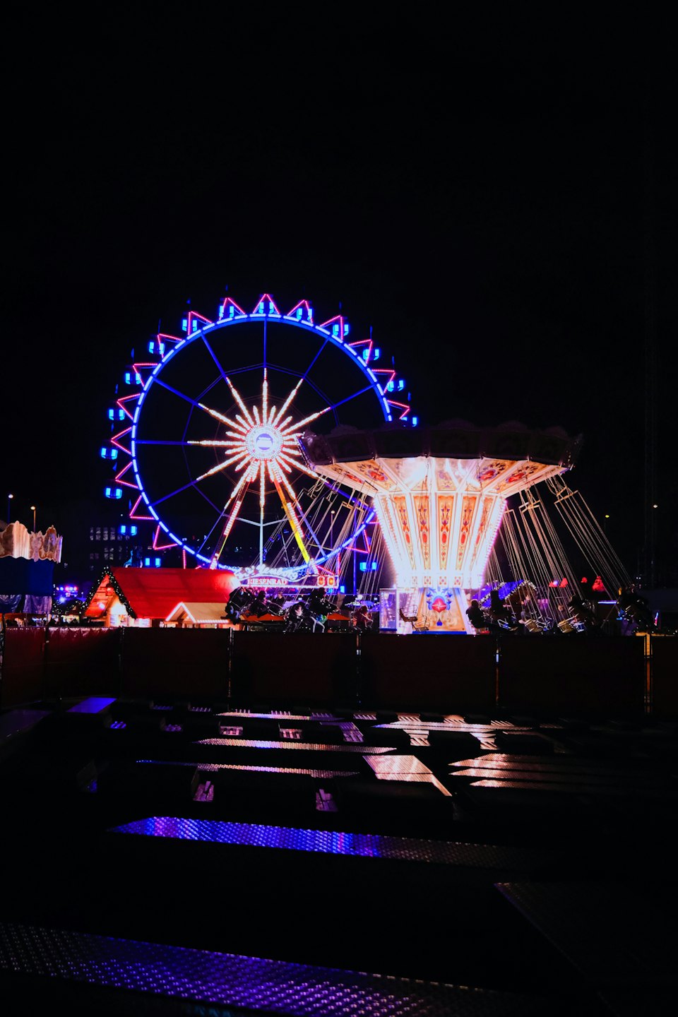 Leuchtendes Riesenrad und schwingende Karussellfahrt auf einem nächtlichen Jahrmarkt.