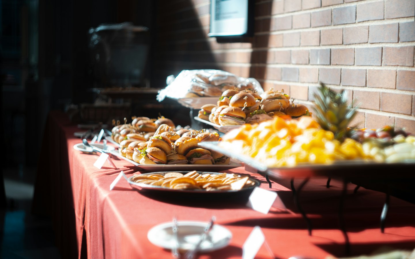 Buffettisch mit Mini-Sandwiches und Obstplatten vor einer Ziegelwand.