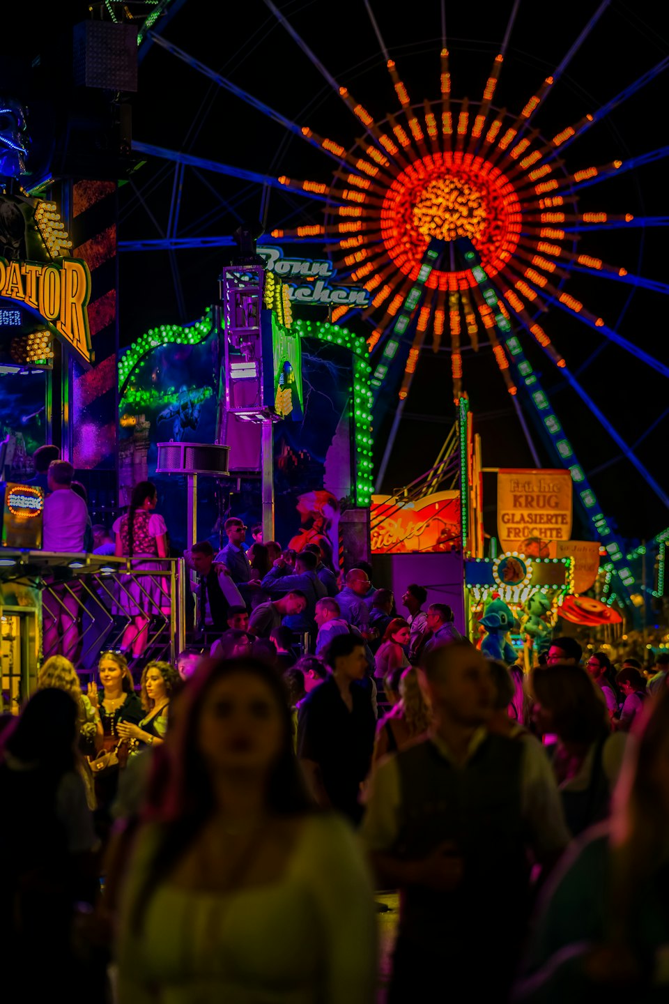 Menschenmengen schlendern durch einen Jahrmarkt mit einem großen, beleuchteten Riesenrad.