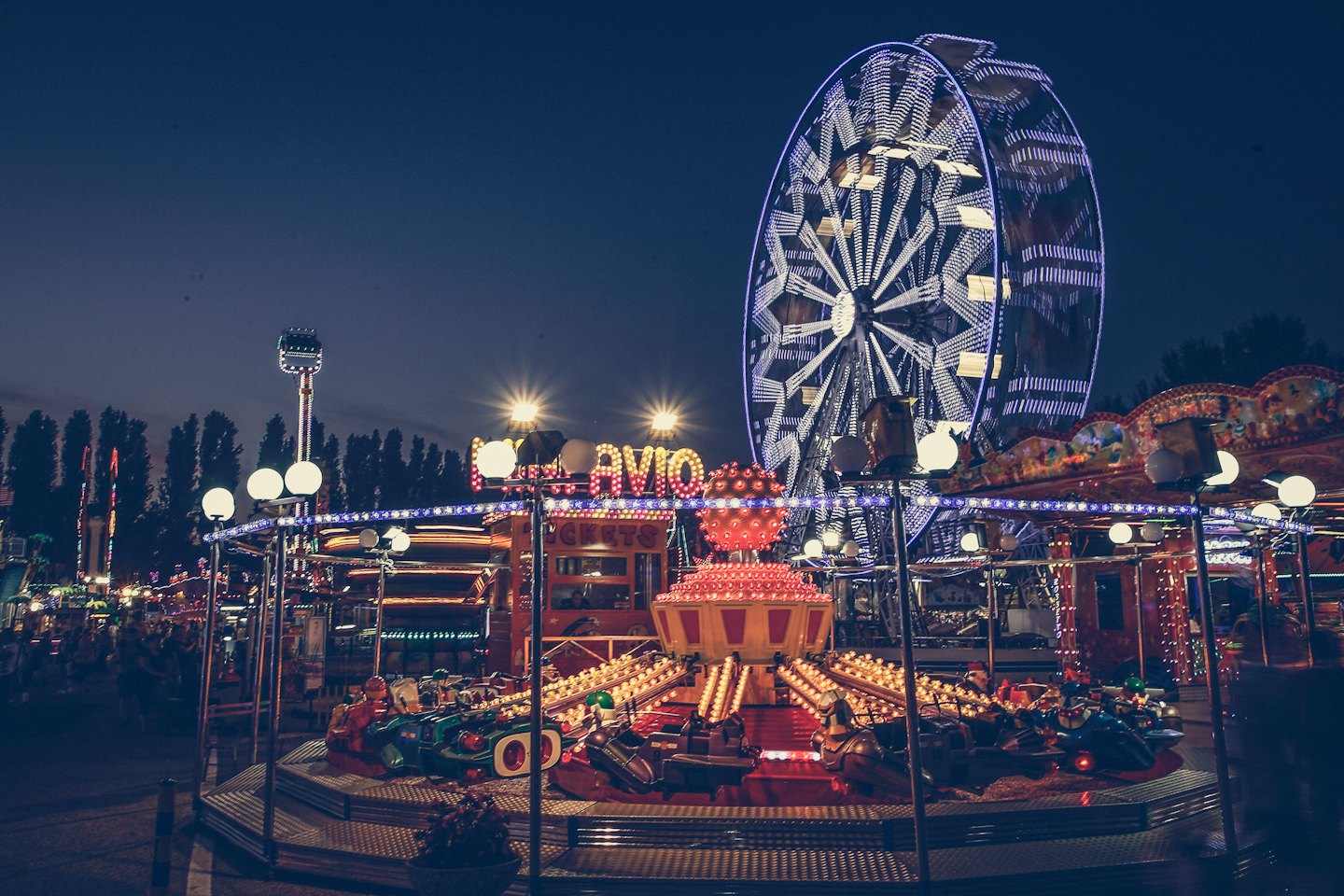 Ein beleuchtetes Riesenrad steht über einer sich drehenden Vergnügungsfahrt.