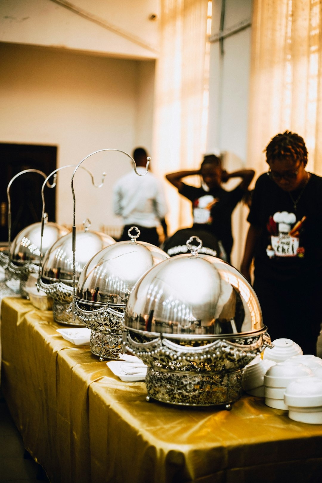 Catering buffet with silver chafing dishes on a golden tablecloth.